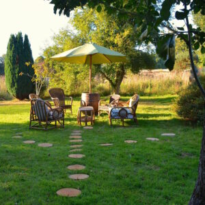 Un jardin zen avec des pas en rondin de bois, un salon vintage en osier et un parasol tonneau.