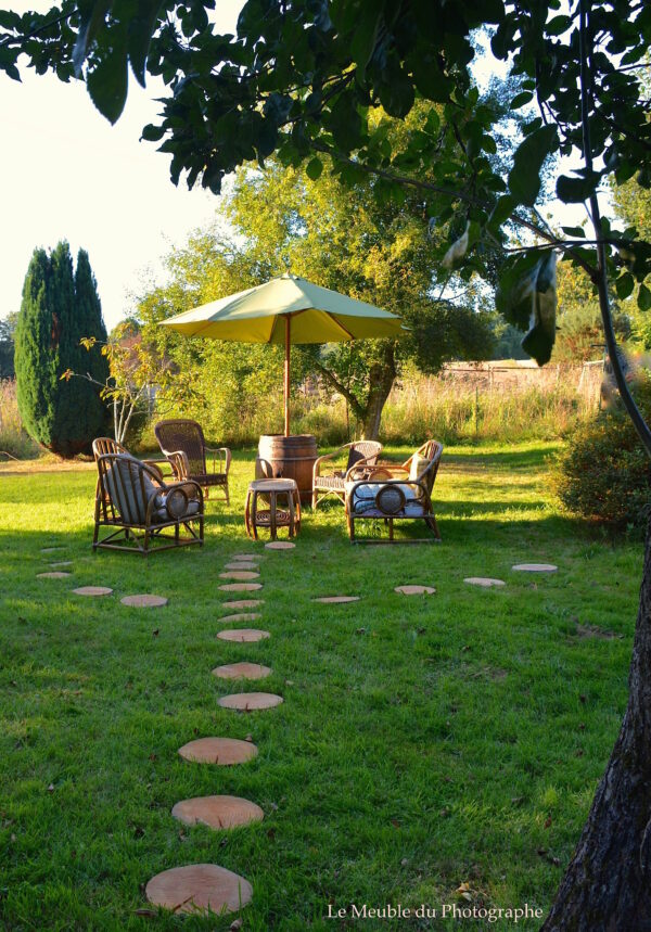 Un jardin zen avec des pas en rondin de bois, un salon vintage en osier et un parasol tonneau.